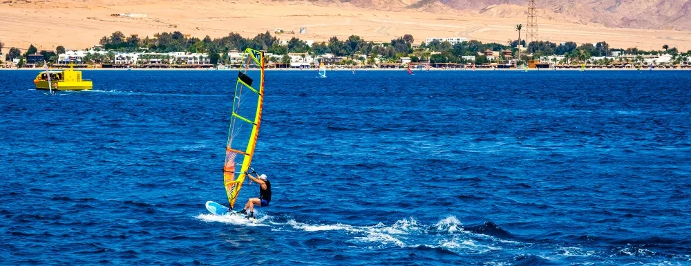 man_with_extreme_windsurfing_sport_blue_sea_with_sand_beach_background.