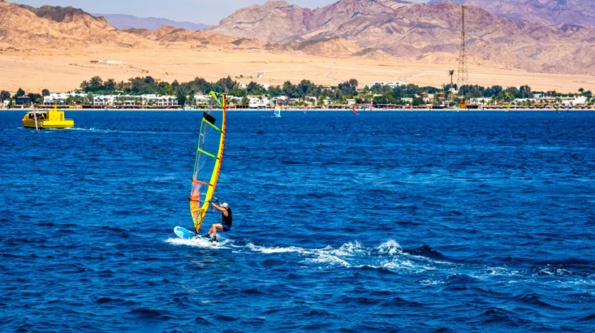 man_with_extreme_windsurfing_sport_blue_sea_with_sand_beach_background.